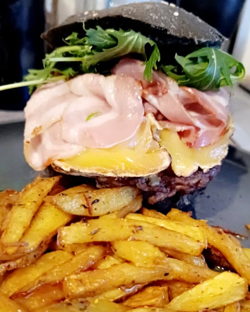 Burger au pain noir garni de jambon, fromage fondu et roquette, accompagné de frites maison