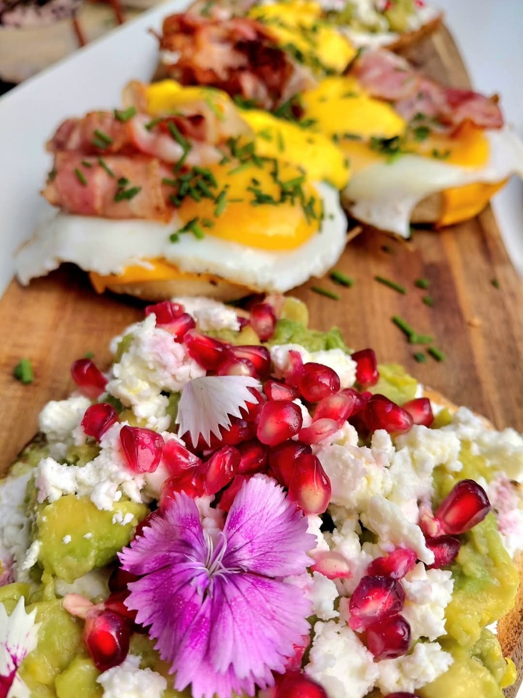 Planche de tartines dressées : œuf au plat et bacon, écrasé d'avocat, feta et grains de grenade