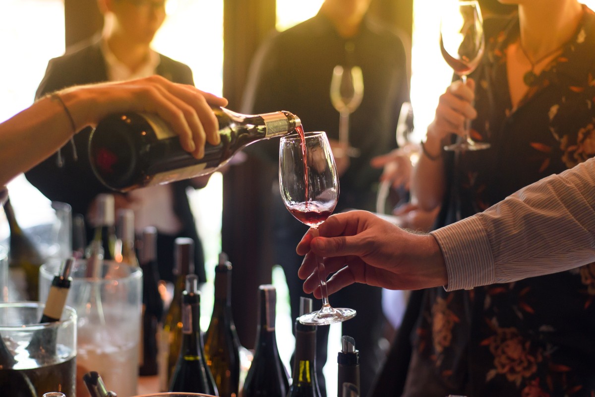 Service de vin rouge dans un verre lors d'une dégustation, plusieurs bouteilles ouvertes au premier plan