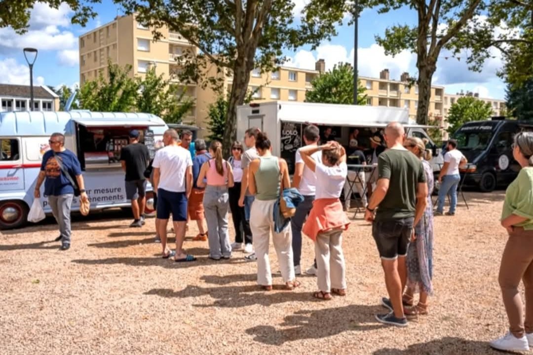 L'Estafette bleu clair de L'Épicurienne stationnée sur une place ombragée, entourée de clients venus commander