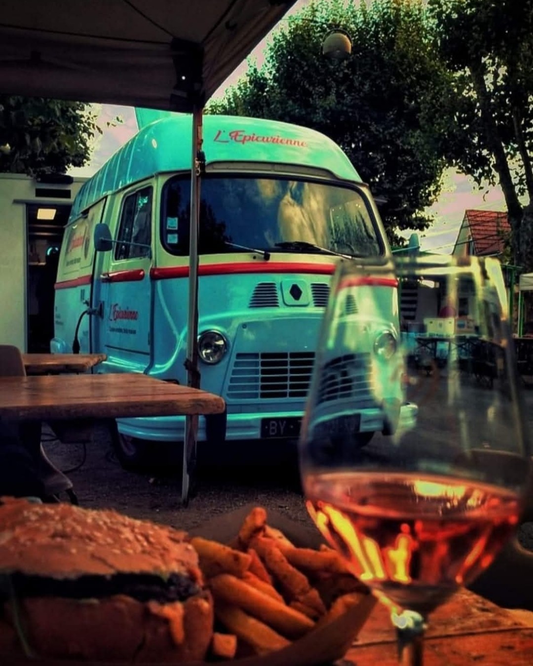 L'Estafette de L'Épicurienne garée sous les arbres au crépuscule, vue depuis une table avec un burger, des frites et un verre de rosé