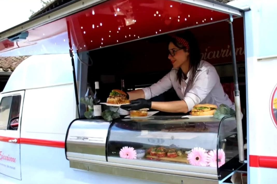 Océane, en veste de cuisine, dresse des assiettes de burgers derrière la vitrine réfrigérée de son camion