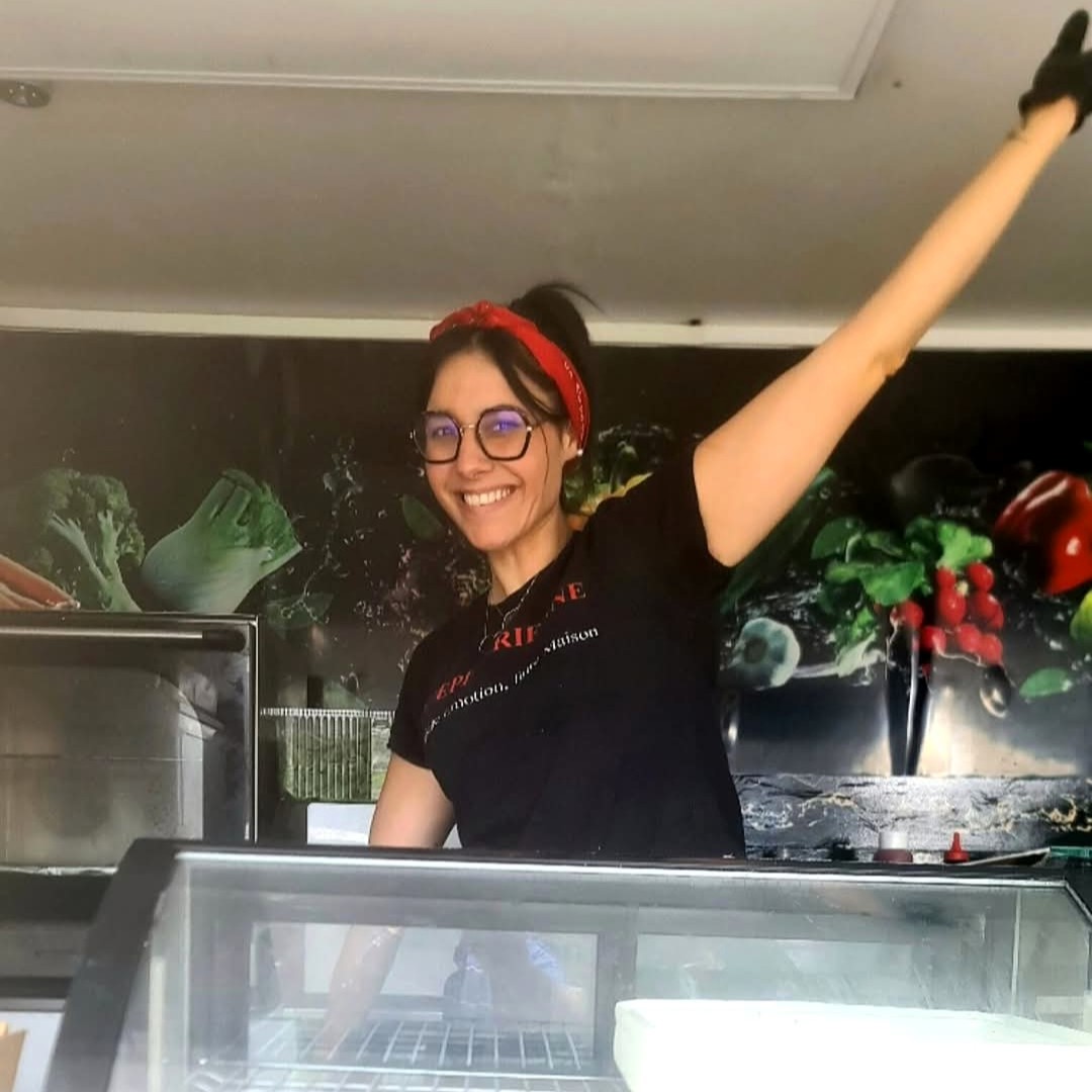 Océane, souriante et le bras levé, derrière la vitrine réfrigérée à l'intérieur de son camion
